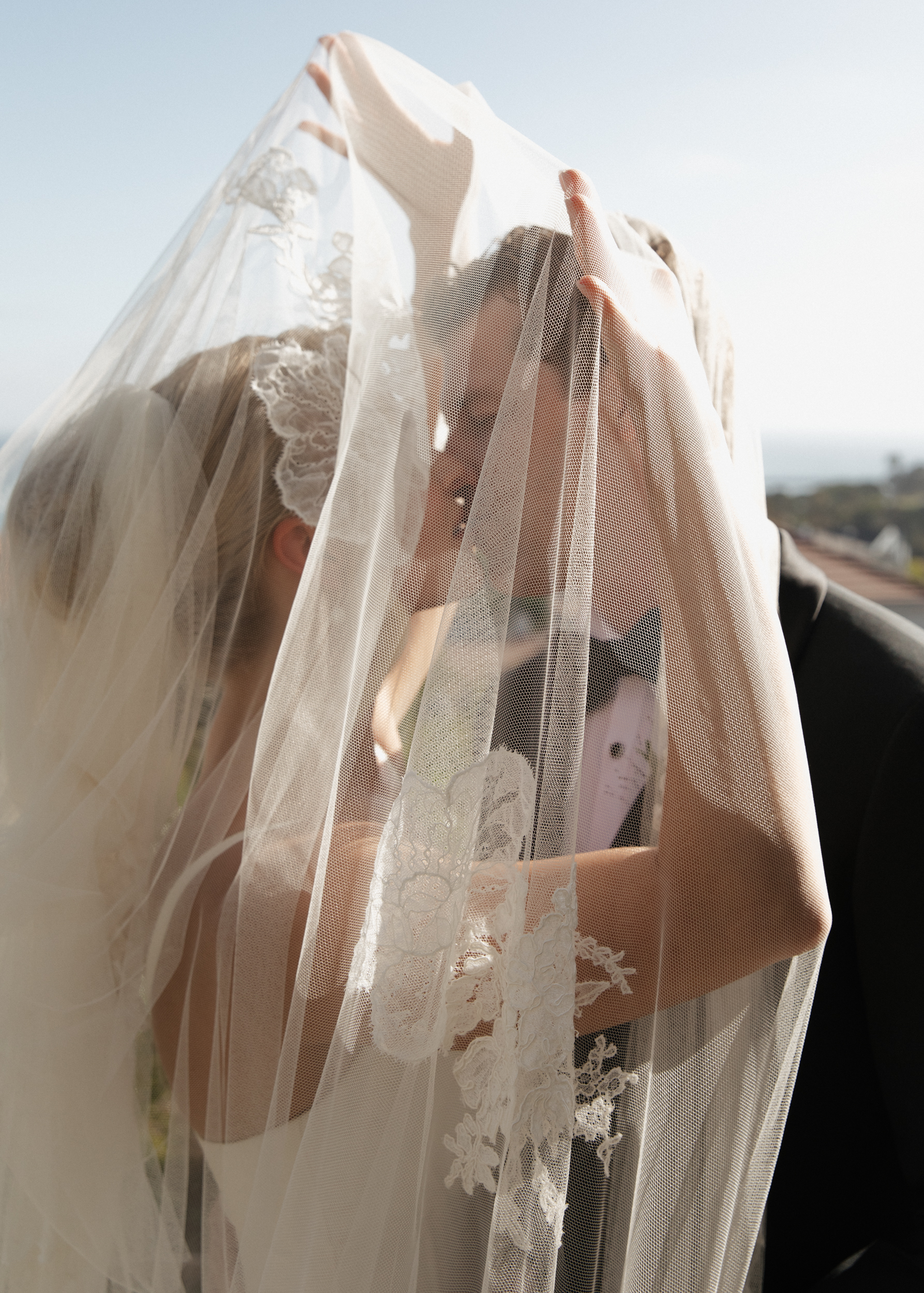 close up image of the bride and groom under a lace detailed veil during sunset, sharing a soft kiss after the wedding ceremony.