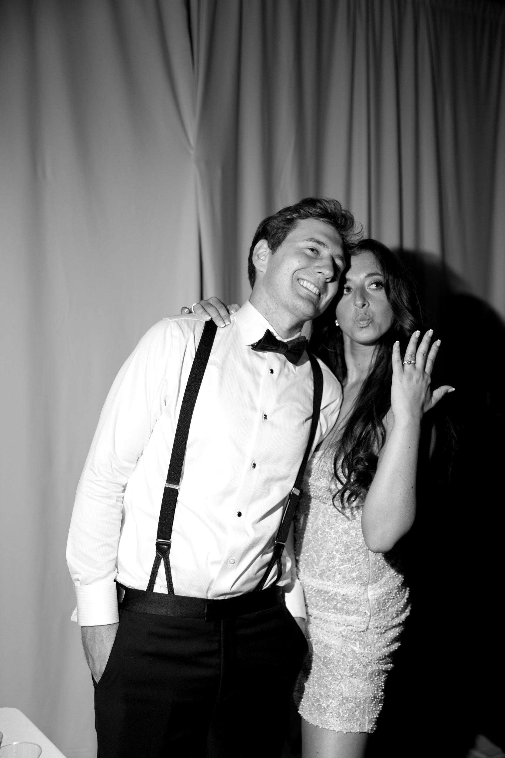 bride and groom smiling just past the camera showing the ring off to family and friends in front of a drapery backdrop